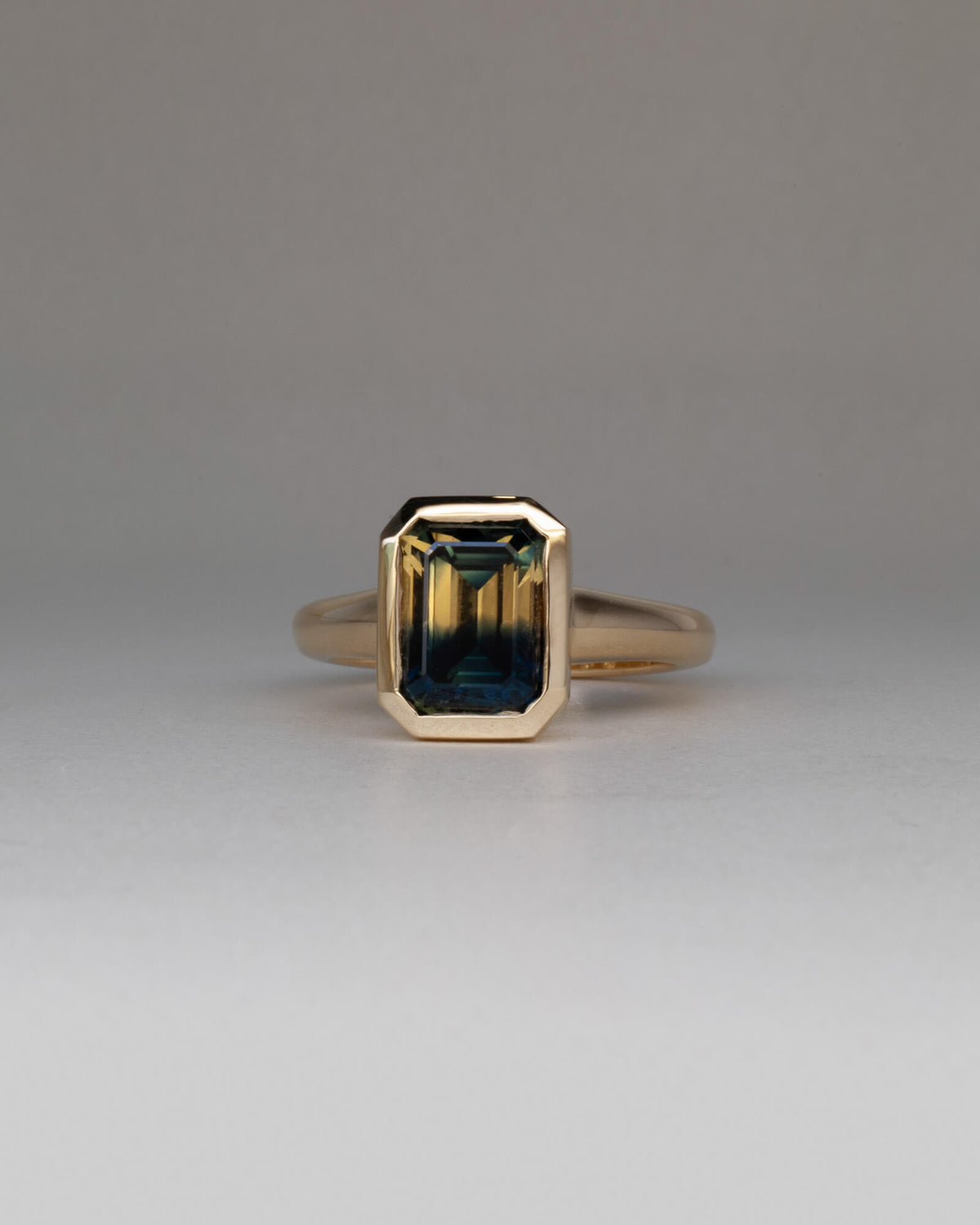 Bespoke Maia emerald cut bezel solitaire engagement ring in 18K yellow gold with 3.37ct Australian parti sapphire — handcrafted by Benjamin Rose Melbourne