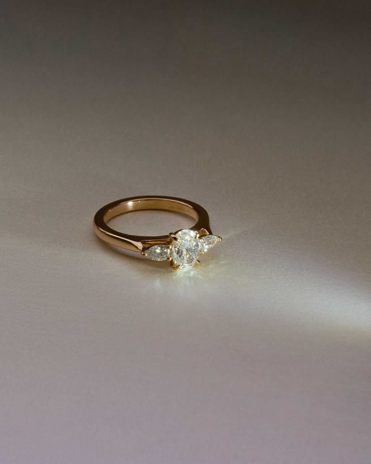 Bespoke oval and pear trilogy engagement ring in 18K yellow gold with 0.81ct natural oval diamond and pear cut diamond side stones — handcrafted by Benjamin Rose Melbourne
