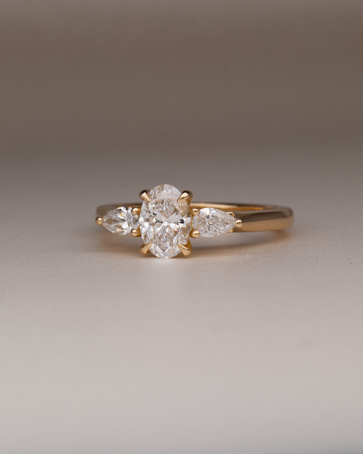 Bespoke oval and pear trilogy engagement ring in 18K yellow gold with 0.81ct natural oval diamond and pear cut diamond side stones — handcrafted by Benjamin Rose Melbourne