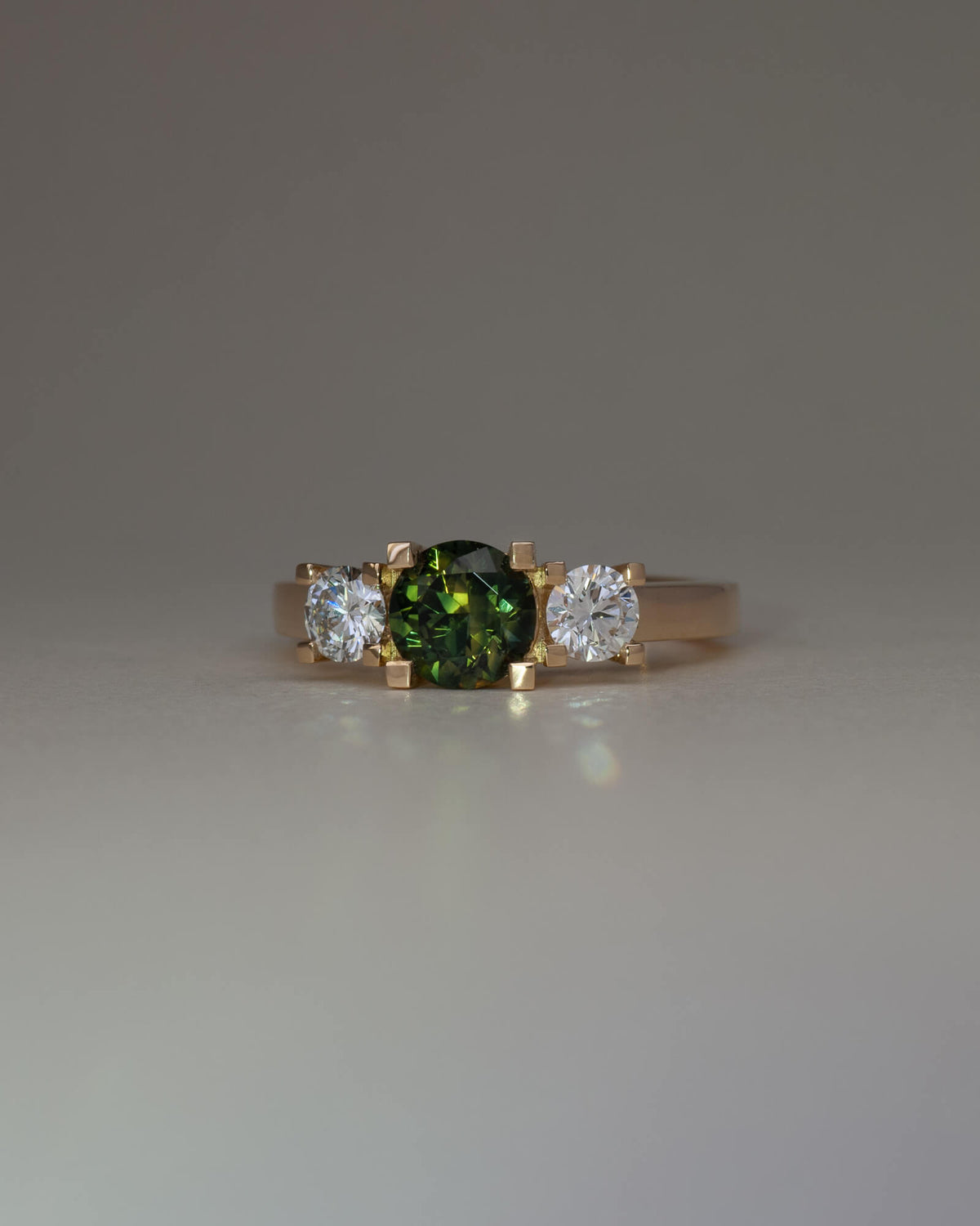 Bespoke square claw trilogy engagement ring in 18K yellow gold with 1.23ct round Australian sapphire and round brilliant lab diamond side stones — handcrafted by Benjamin Rose Melbourne